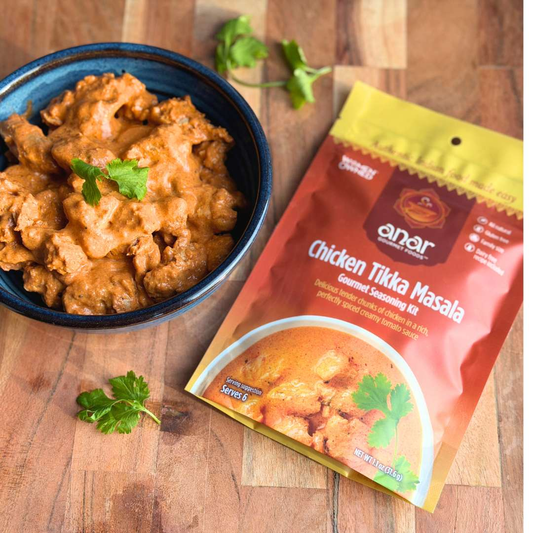 Bowl of Chicken Tikka Masala with Anar Gourmet Foods Chicken Tikka Masala all natural, gluten free seasonings packet on a wooden surface.