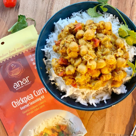 Bowl of chickpea curry and white rice with Anar Gourmet Foods all natural, gluten-free seasoning packet on a wooden surface.