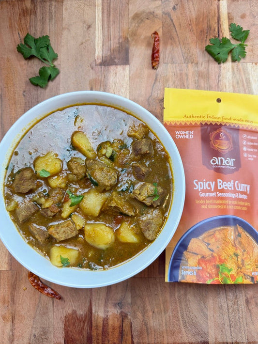 Anar Gourmet Foods all-natural, gluten-free spicy beef curry with potatoes, plated beside seasoning package on a wood board