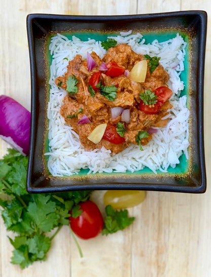 Chicken Tikka Masala served over basmati rice, garnished with fresh tomato, red onion, cilantro, and lime