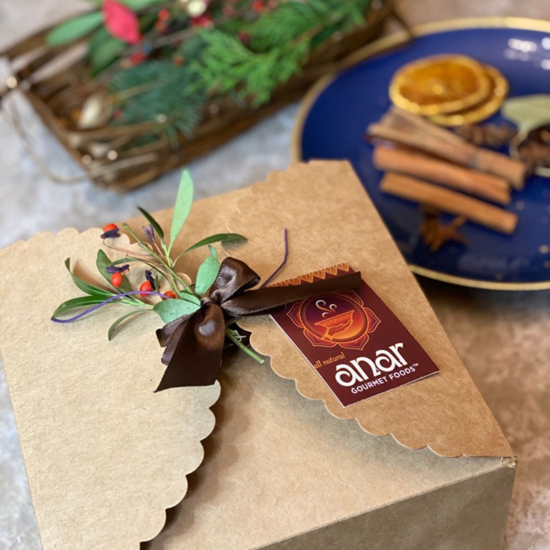 Anar Gourmet Foods meat lovers gift box — closed kraft box with ribbon, greenery, and branded tag, cinnamon and dried orange in background